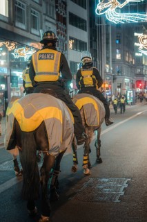 Police officers on horses patrol a brightly lit city street at night, London, England, Great