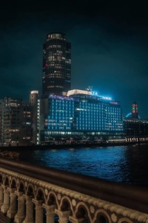 A towering, illuminated building on the riverbank at night against a dark sky, London, England,