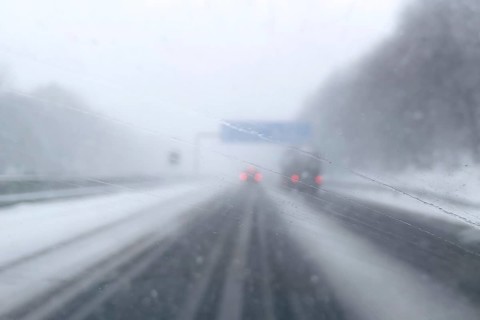 View through fogged windshield of cars driving through light snowblowing on partially covered