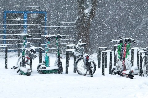 Tailored parked e-scooters and bicycles in winter during snowfall with snowflakes in the picture,
