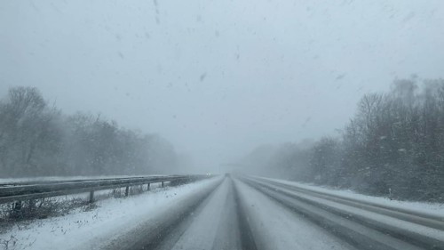 View through the windshield of a passenger car driving through light snow on an empty, partially
