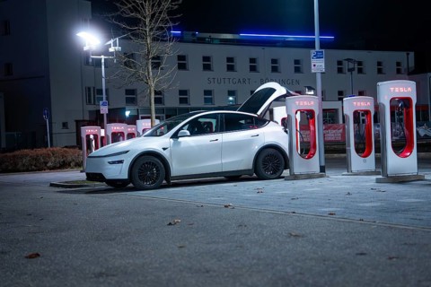 Parking lot with white Tesla at night, open rear, charging stations in the background, Tesla