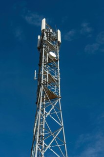 Tall silver telecommunications tower extends to a blue sky with wispy clouds on a sunny dayA tall