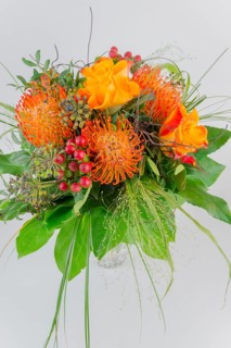 Colorful bouquet in a vase with orange and yellow flowers, red berries and green leaves, protea,