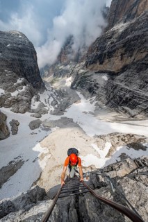 Mountaineer climbs a ladder in steep rocky terrain, Via Ferrata Oliva Detassis via ferrata, view of