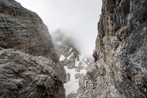 Mountaineer climbs the Via Ferrata Oliva Detassis via ferrata, steep cliffs covered in clouds,
