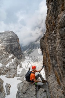 Mountaineer climbs the Via Ferrata Oliva Detassis via ferrata, view of mountain basin with steep