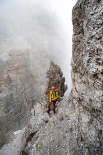 Mountaineer climbs the Via Ferrata Oliva Detassis via ferrata in fog, steep mountains covered in