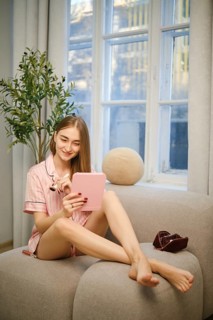 Beauty blogger sits on a couch with her legs crossed while using a tablet. She talks about the