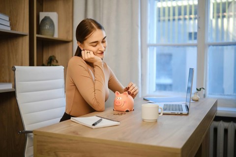 A woman is sitting at her desk in an office. She looks thoughtful while holding her chin in one