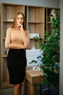 A woman stands in an office with wooden shelves behind her. She has long hair and wears a fitted