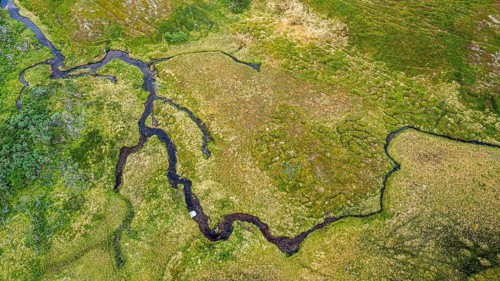 Aerial view of green fells and moorland crossed by streams, river traversing lush, green landscape