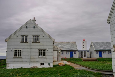 Lighthouse between blue and white houses rises under a grey sky Kjølnes Fyr, small windows and