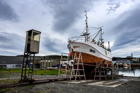 A large boat fishing trawler fishing vessel on a dry dock is positioned against a cloudy sky in the