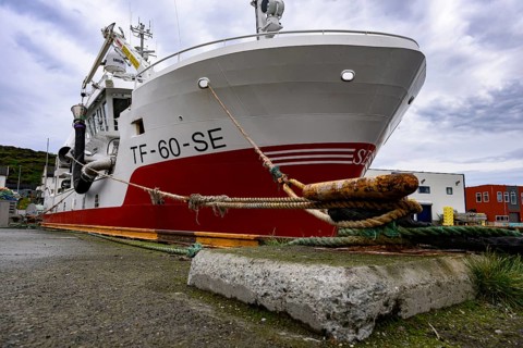 Large fishing boat fishing vessel in harbor secured by thick ropes cords on a massive