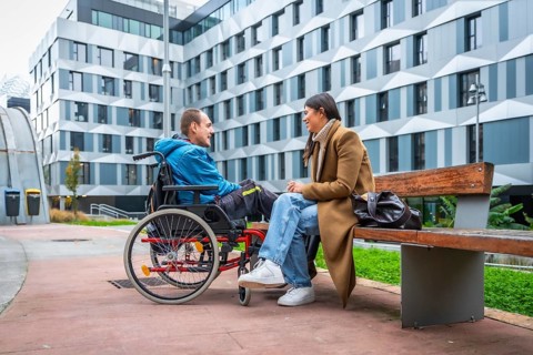 Young man living with a disability sitting in a wheelchair and having a joyful conversation with a