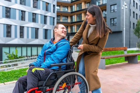 Woman companion assisting a smiling man using a wheelchair, enjoying a happy moment together in an
