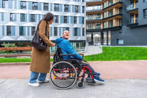 Caregiver pushing a happy adult man with a disability in a wheelchair, enjoying time outdoors