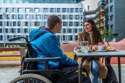 Man with disability in wheelchair talking with female friend while having coffee and pastry at an