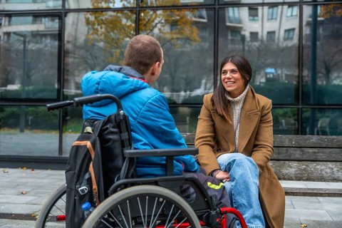 Disabled man seated in a wheelchair engaging in a joyful conversation with a supportive woman on a