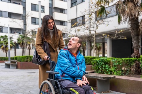 Woman pushing an adult man in a wheelchair, providing support and care during an urban outing,
