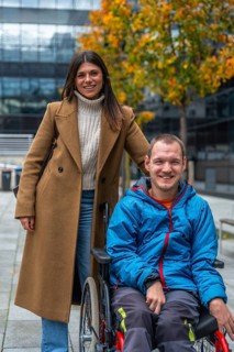 Young woman pushes her smiling partner in a wheelchair along an accessible urban pathway amid