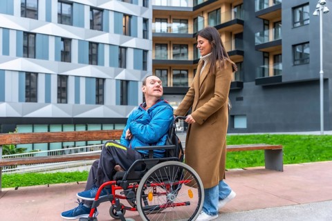 Young woman smiling as she pushes a man in a wheelchair along an accessible city street, showcasing
