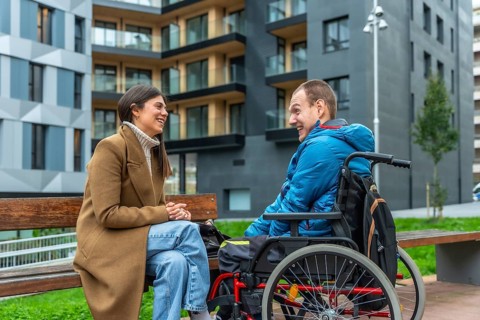 Happy young woman sitting on a bench, engaging in conversation and laughing with a smiling man