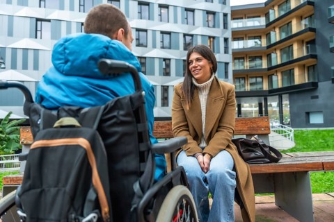 Woman on urban bench smiling and listening attentively to man in wheelchair, sharing supportive