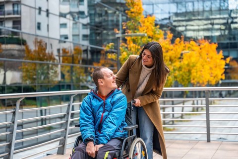Support worker assisting a smiling disabled man in a wheelchair on an autumn day, navigating an
