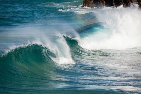 Waves crash against rocks at the mainland's easternmost point, creating rainbows in the ocean spray