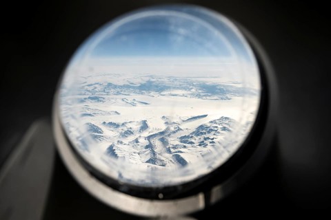 View from an airplane window of snowy arctic mountain landscape with glaciers, aerial view,