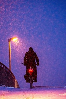 Winter weather, blowing snow, person with e-bike, bicycle on snowy bridge, footpath bridge, steep