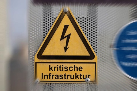 (Photo montage) Text CRITICAL INFRASTRUCTURE on a warning sign for a high-voltage line