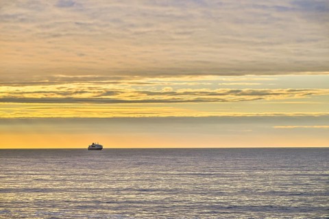 A Hurtigrute ship on the wide Barents Sea at sunset midnight sun, yellowish clouds and calm seas,