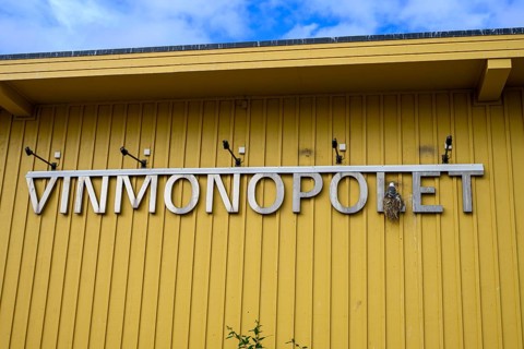 Yellow building of the Norwegian state wine monopoly with sign and floodlights and a breeding