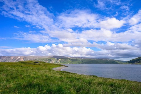 Green meadows on the banks of Syltefjord with clouds in the blue sky, landscape with a lake and