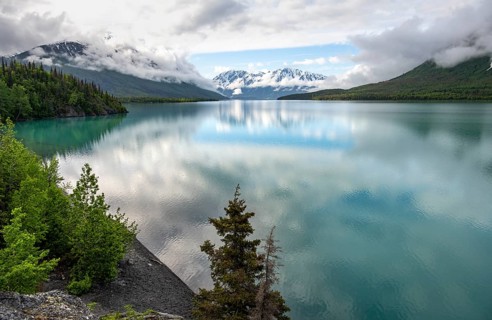 Snowy mountains in spring are reflected in turquoise blue Kenai Lake, Cooper Landing, Kenai