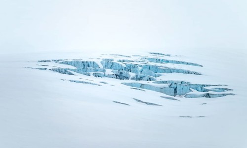 Smooth white snowy area on the glacier broken by crevasses with blue rugged glacial ice, detail,