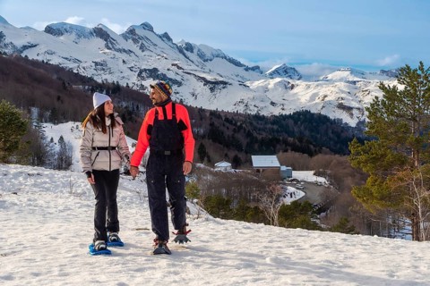 Couple snowshoeing hand in hand through fresh pyrenees snow, smiling and enjoying a sunny winter