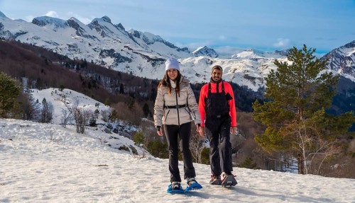 Couple snowshoeing on a snowy mountain trail, smiling and looking at the camera, with majestic snow