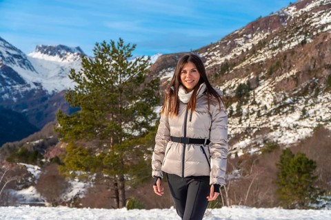 Young woman smiling and walking through snowy mountain landscape, wearing a warm jacket and scarf