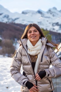 Young woman smiling while adjusting her warm winter jacket with a scarf, standing outdoors against