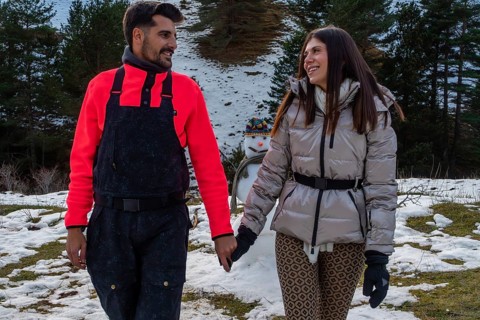 Smiling young couple enjoying a winter walk in the snowy mountains, hand in hand, with a snowman
