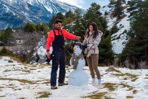 Young couple joyfully building a snowman together in a snowy mountain landscape, celebrating winter