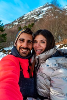 Smiling young man and woman capturing a selfie together during a snowy winter vacation, enjoying