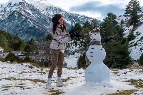 Young woman actively building a snowman outdoors with snow capped mountains and pine trees in the