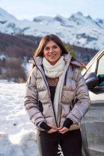 Young woman smiling while zipping up her warm jacket, standing outdoors in a snowy mountain