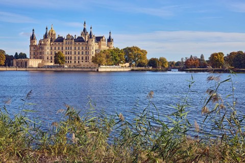 Castle, lake Burgsee, reed (Phragmites australis), trees, bushes, water surface with small waves,