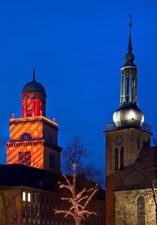 The Christmassy illuminated town hall tower and the illuminated church tower of St. John's Church